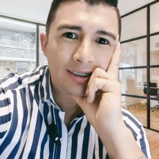 Edgar Jaimes sonriente con camisa a rayas azules y blancas, con brackets en los dientes, posando en una oficina moderna con paredes de vidrio.